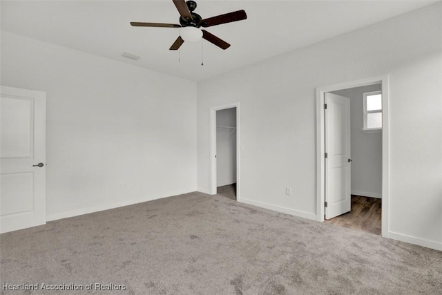 unfurnished bedroom featuring ceiling fan, light colored carpet, a walk in closet, and a closet