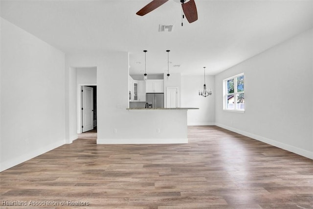 unfurnished living room featuring ceiling fan with notable chandelier and light hardwood / wood-style flooring