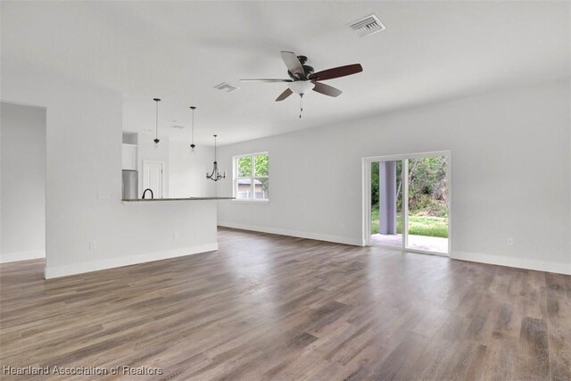 unfurnished living room with plenty of natural light, ceiling fan with notable chandelier, and dark wood-type flooring