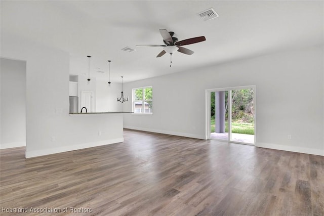 unfurnished living room with ceiling fan with notable chandelier, dark wood-type flooring, and a healthy amount of sunlight