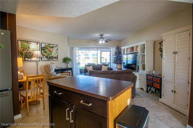 kitchen featuring ceiling fan, a center island, dark brown cabinetry, a textured ceiling, and stainless steel fridge