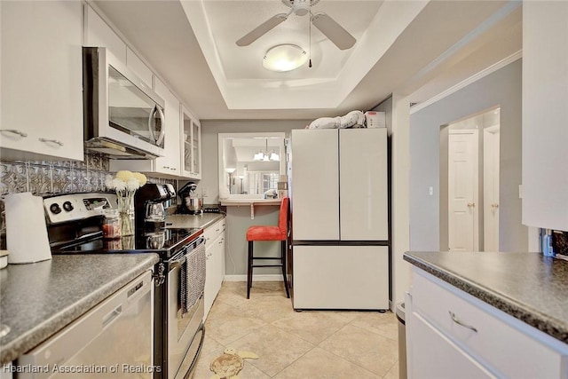 kitchen with ceiling fan, appliances with stainless steel finishes, white cabinets, light tile patterned floors, and a tray ceiling