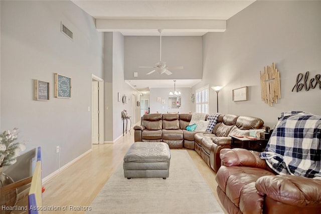 living room with ceiling fan with notable chandelier, light hardwood / wood-style flooring, beamed ceiling, and a high ceiling