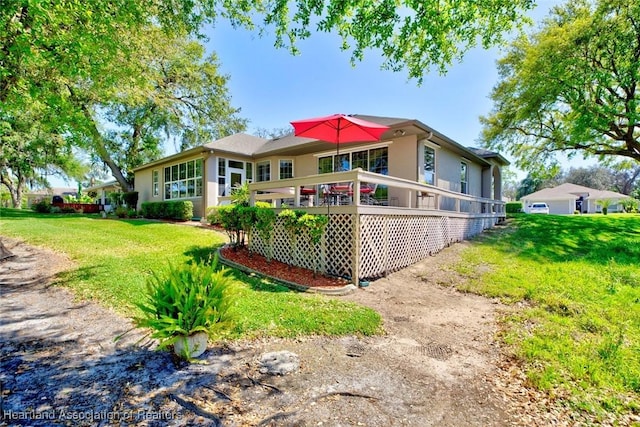 rear view of house featuring a wooden deck, a yard, and stucco siding