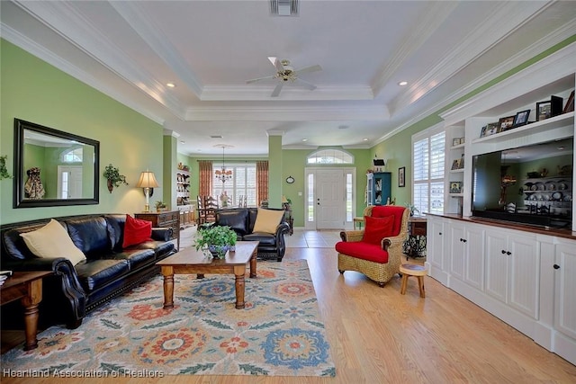 living area featuring visible vents, ceiling fan with notable chandelier, a tray ceiling, light wood-style floors, and crown molding