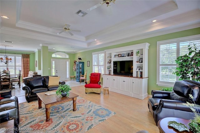 living area with light wood-type flooring, visible vents, ornamental molding, a raised ceiling, and ceiling fan