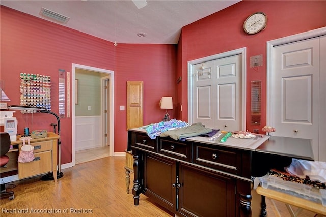 bedroom featuring a ceiling fan, visible vents, light wood finished floors, and wainscoting