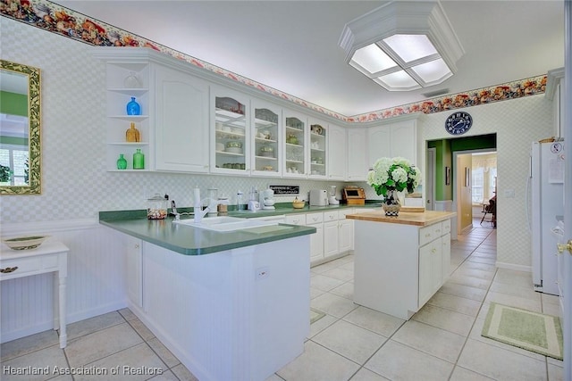 kitchen featuring a sink, white cabinetry, a peninsula, wallpapered walls, and glass insert cabinets