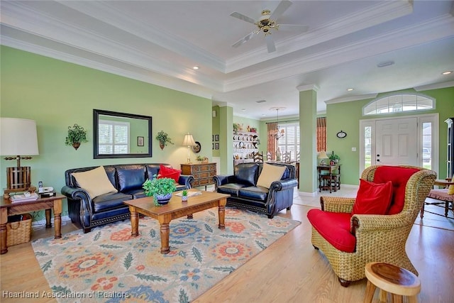 living area with a raised ceiling, crown molding, wood finished floors, and ornate columns