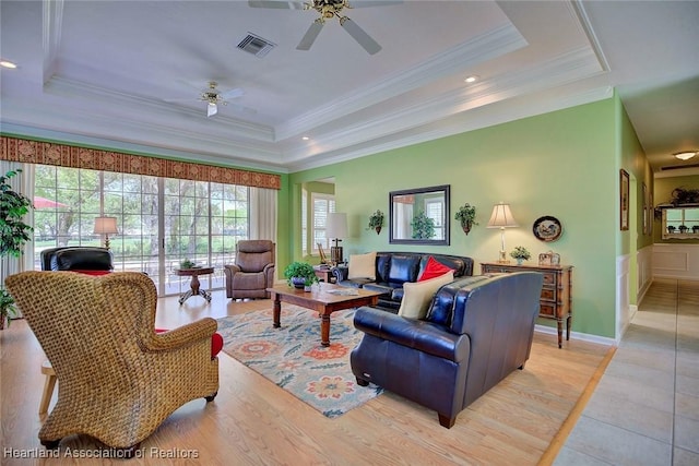 living room featuring a ceiling fan, a tray ceiling, crown molding, and visible vents