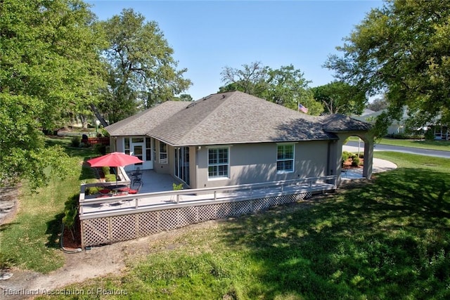 rear view of house featuring a deck, a lawn, a shingled roof, and stucco siding