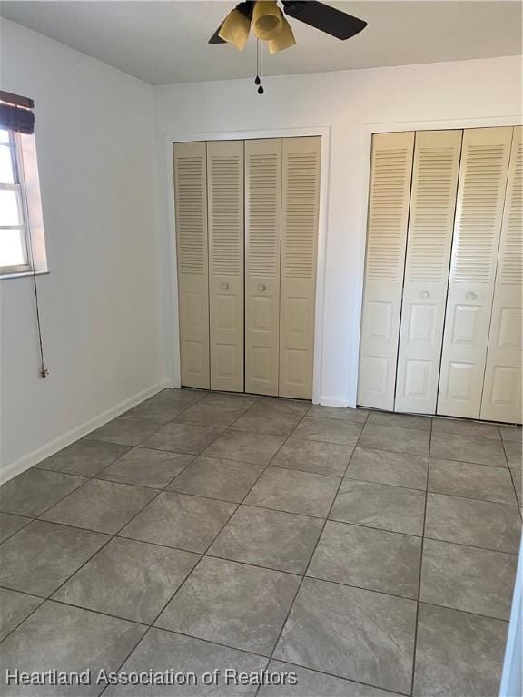 unfurnished bedroom featuring ceiling fan, tile patterned floors, and two closets