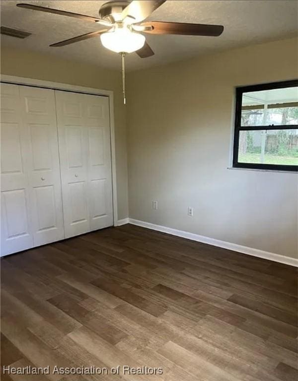 unfurnished bedroom featuring dark wood-type flooring, a closet, and ceiling fan