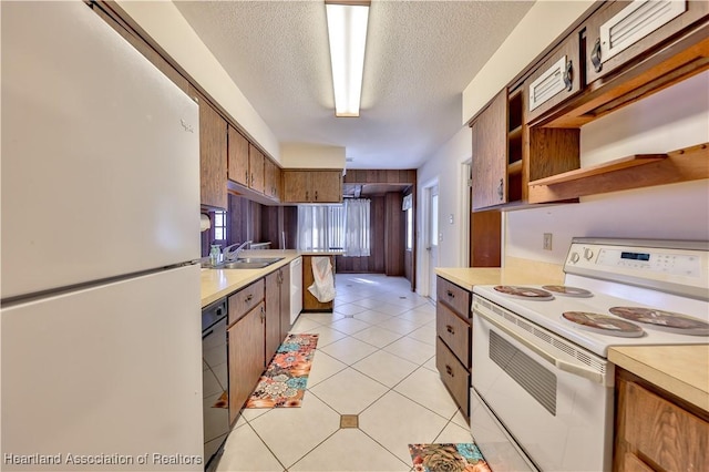 kitchen with light tile patterned flooring, a textured ceiling, white appliances, and sink