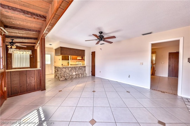 unfurnished living room with tile patterned flooring, ceiling fan, and beamed ceiling