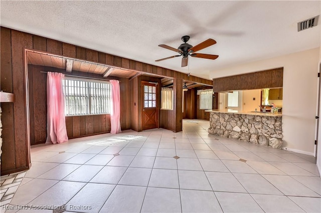 unfurnished living room with a textured ceiling, ceiling fan, wooden walls, and light tile patterned flooring