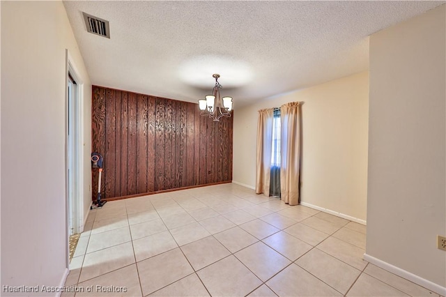 spare room with a textured ceiling, an inviting chandelier, wooden walls, and light tile patterned flooring