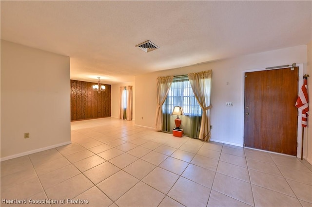 unfurnished room with wood walls, light tile patterned floors, and an inviting chandelier