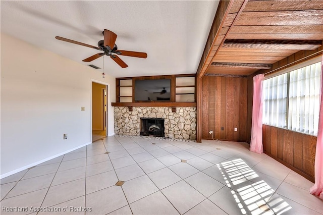 unfurnished living room with a stone fireplace, wood walls, ceiling fan, and light tile patterned floors