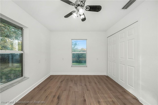 unfurnished bedroom featuring multiple windows, a closet, dark hardwood / wood-style floors, and ceiling fan