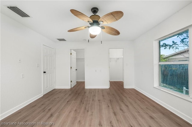 unfurnished bedroom featuring hardwood / wood-style floors, a closet, a spacious closet, and ceiling fan