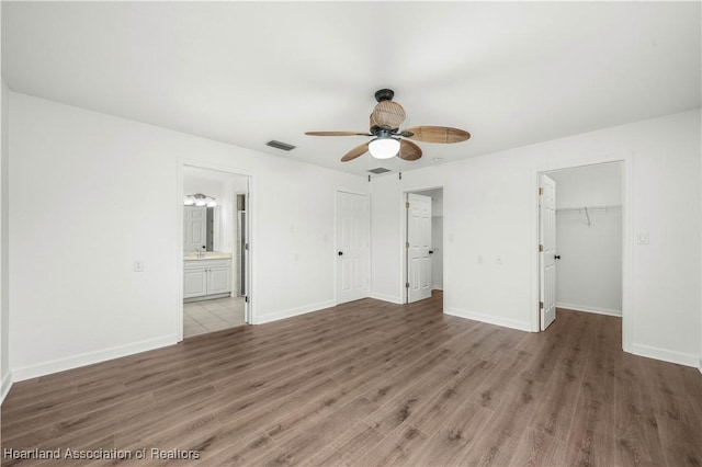 unfurnished bedroom featuring connected bathroom, ceiling fan, a spacious closet, and dark hardwood / wood-style floors