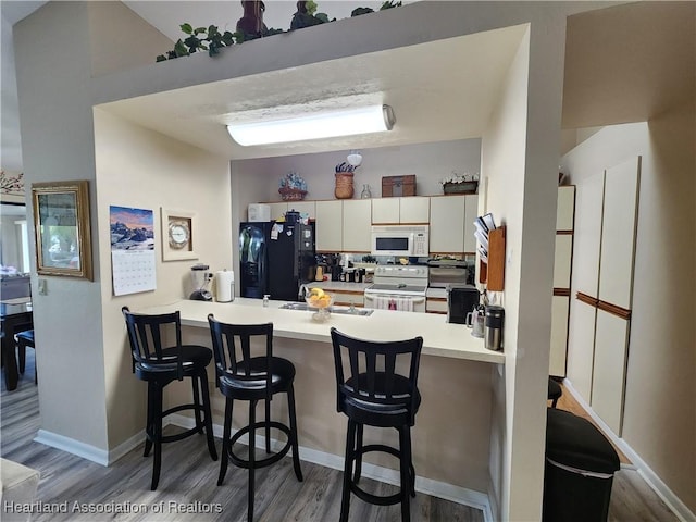 kitchen featuring kitchen peninsula, a breakfast bar, white cabinets, and white appliances