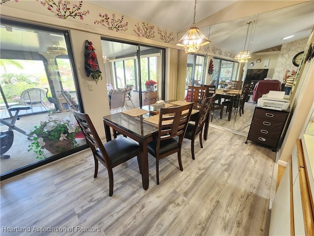 dining area with a chandelier, light wood-type flooring, and vaulted ceiling