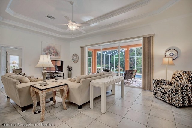 tiled living room with a tray ceiling, a wealth of natural light, ceiling fan, and ornamental molding