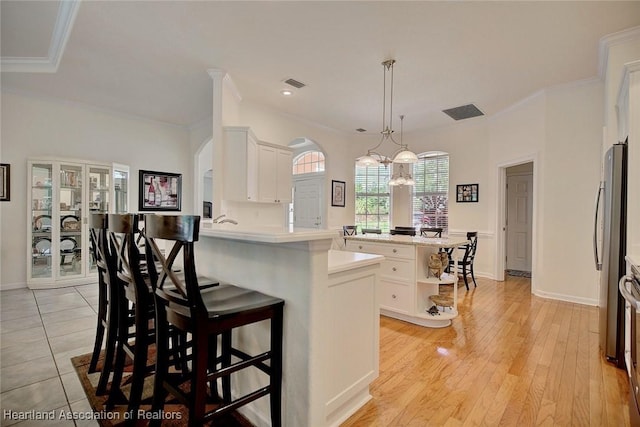 kitchen featuring kitchen peninsula, a kitchen bar, decorative light fixtures, white cabinets, and a center island