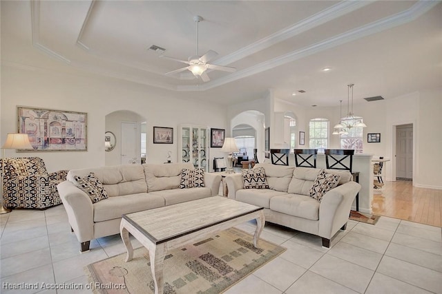 living room featuring light tile patterned floors, ceiling fan with notable chandelier, a raised ceiling, and crown molding