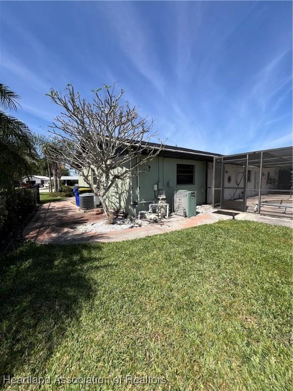 back of house with glass enclosure, a patio, a lawn, and central AC