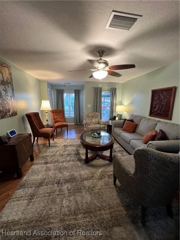 living room featuring visible vents, ceiling fan, a textured ceiling, and wood finished floors