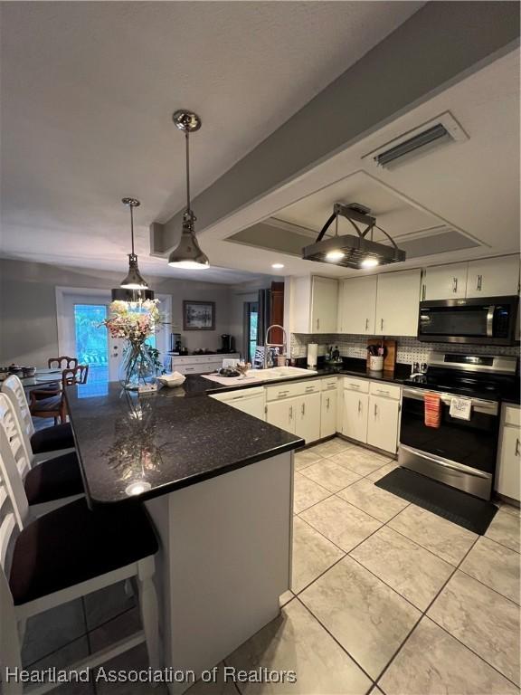 kitchen with appliances with stainless steel finishes, dark countertops, white cabinets, and a peninsula