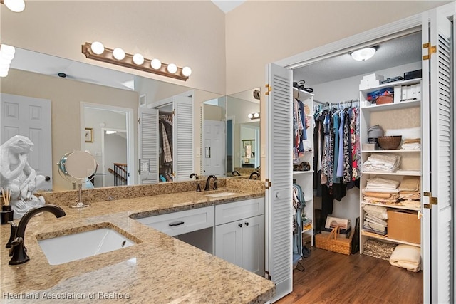 full bath with a sink, double vanity, wood finished floors, and a spacious closet