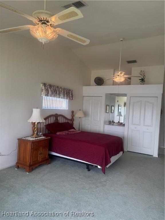 bedroom with visible vents, two closets, high vaulted ceiling, carpet floors, and ceiling fan