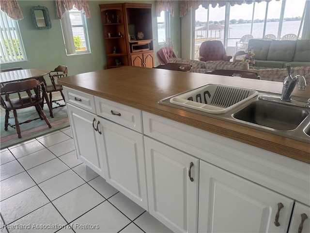 kitchen with dark countertops, open floor plan, light tile patterned floors, white cabinets, and a sink