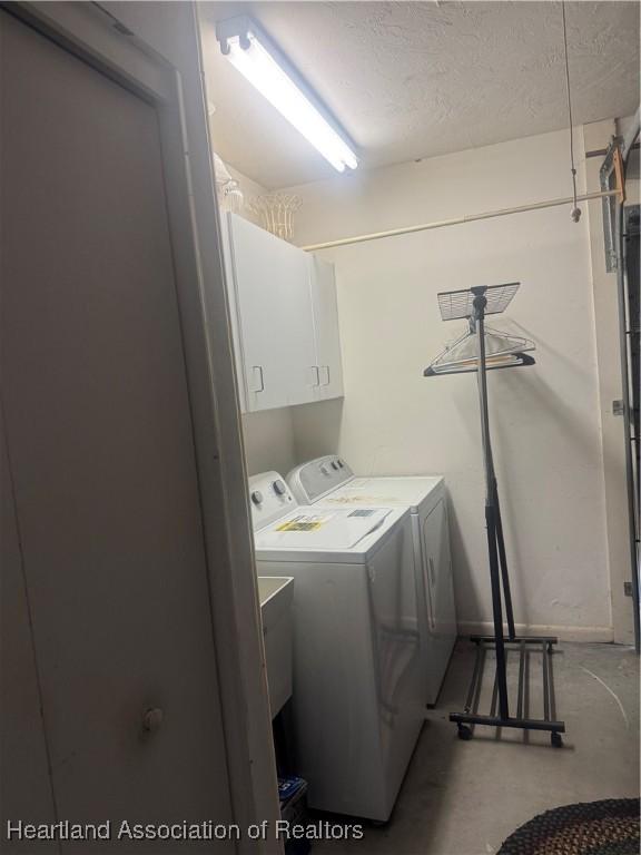 washroom featuring cabinet space, washing machine and dryer, and a textured ceiling