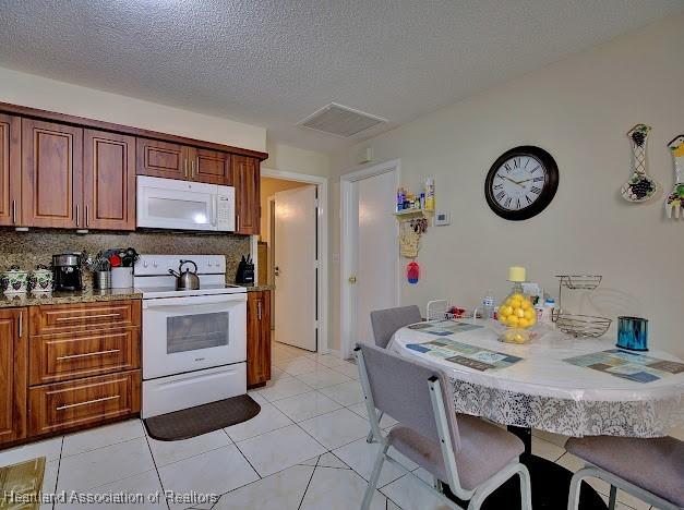 kitchen with backsplash, a textured ceiling, light tile patterned floors, and white appliances