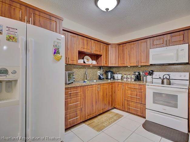 kitchen featuring white appliances, light stone countertops, a textured ceiling, light tile patterned floors, and tasteful backsplash