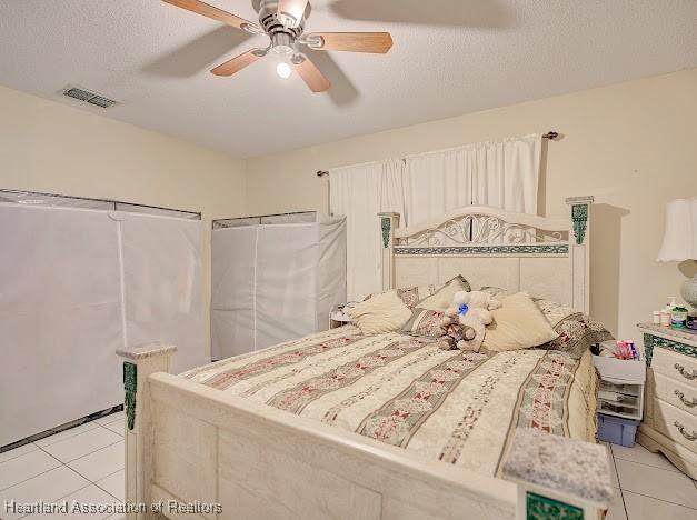 bedroom with ceiling fan, light tile patterned floors, and a textured ceiling