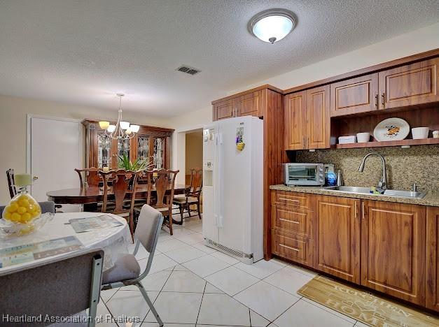 kitchen featuring tasteful backsplash, sink, pendant lighting, a chandelier, and white fridge with ice dispenser