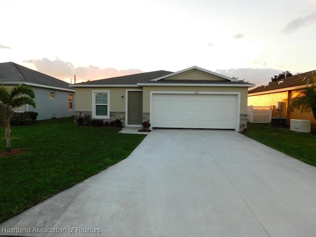 ranch-style house with a garage, a yard, and central AC unit