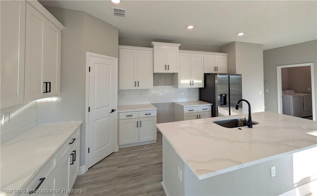 kitchen with independent washer and dryer, stainless steel fridge, sink, and a center island with sink