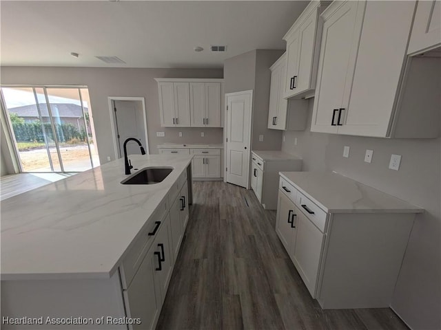 kitchen with dark wood-type flooring, an island with sink, sink, and white cabinets