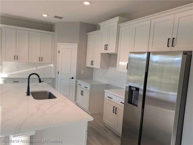 kitchen featuring a kitchen island with sink, stainless steel fridge with ice dispenser, sink, and white cabinets