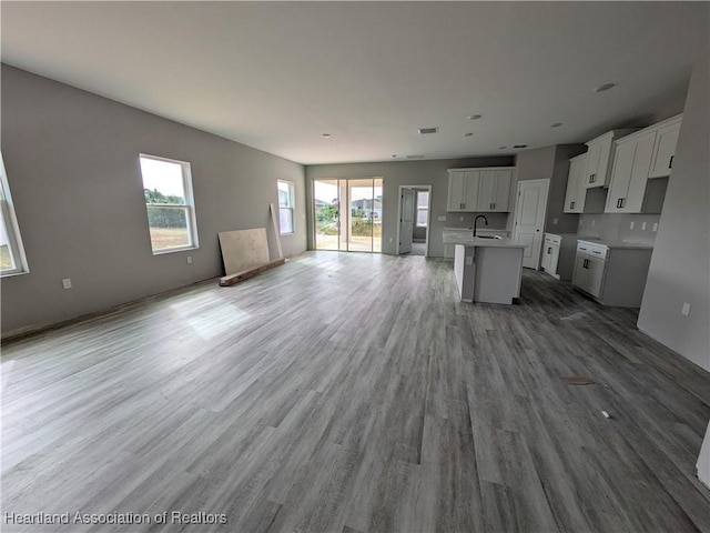 kitchen with hardwood / wood-style flooring, sink, an island with sink, and white cabinets