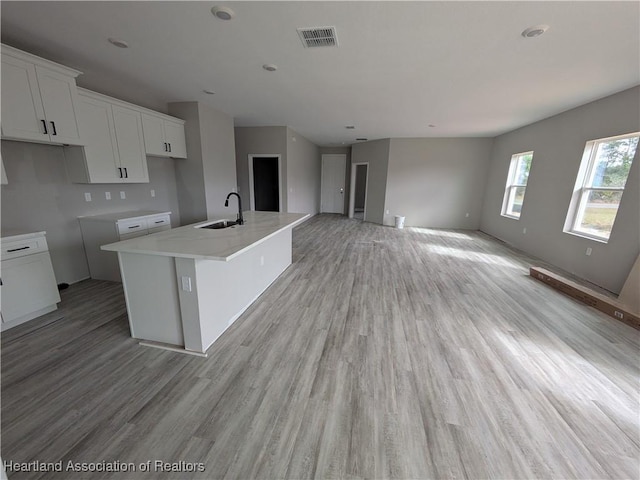 kitchen with sink, white cabinetry, a center island with sink, light hardwood / wood-style flooring, and light stone countertops