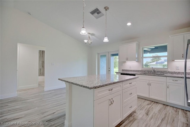 kitchen with french doors, sink, white cabinets, a kitchen island, and hanging light fixtures