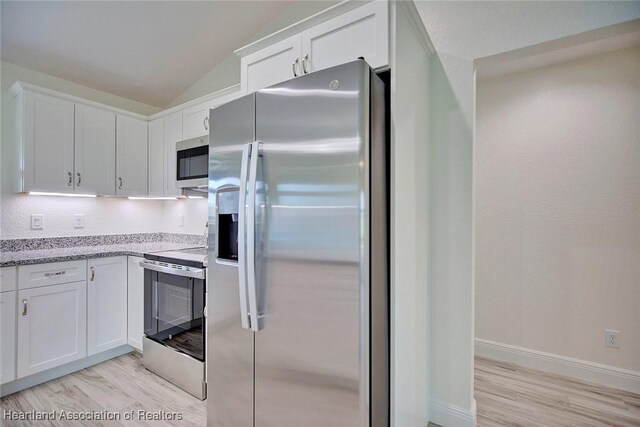 kitchen featuring light stone counters, white cabinetry, stainless steel appliances, and vaulted ceiling